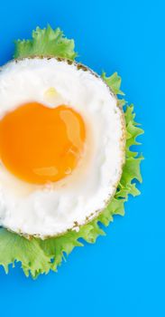 Half of Fried Eggs Sunny Side Up with Lettuce on Blue background. Top View