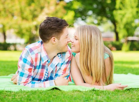 holidays, vacation, love and friendship concept - smiling couple lying on blanket and touching noses in park