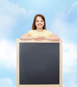 people, advertisement and education concept - happy little girl with blank blackboard