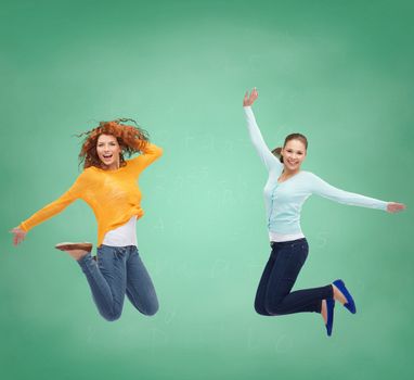 happiness, freedom, friendship, education and people concept - smiling young women jumping in air over green board background