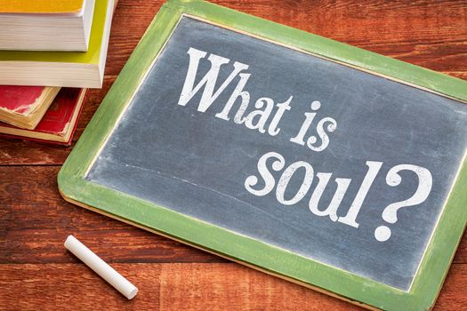 What is soul spiritual question on a slate blackboard with a white chalk and a stack of books against rustic wooden table