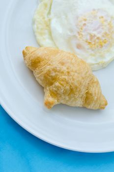 A breakfast croissant with fried egg on dish