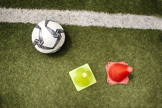 Photograph of a soccer ball and some plastic cones, on an artificial grass field