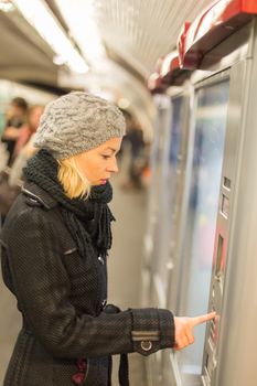 Casually dressed woman wearing winter coat,buying metro ticket at the ticket vending machine. Urban transport.