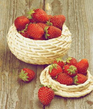 Fresh Ripe Forest Strawberries in Wicker Bowls isolated on Rustic Wooden background. Retro Styled