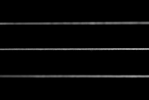 A dramatic 1:1 macro shot of acoustic guitar strings framed horizontally across the frame in black and white.