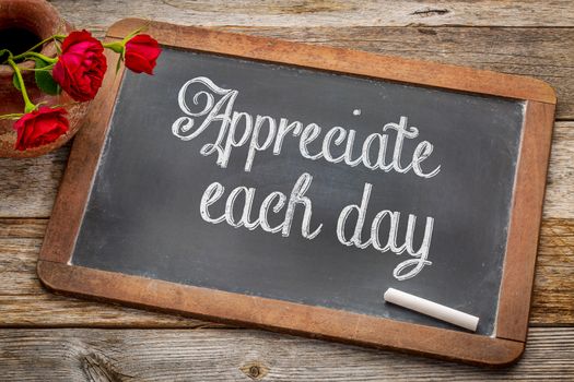 Appreciate each day  - white chalk text on a vintage slate blackboard with red roses against rustic wood