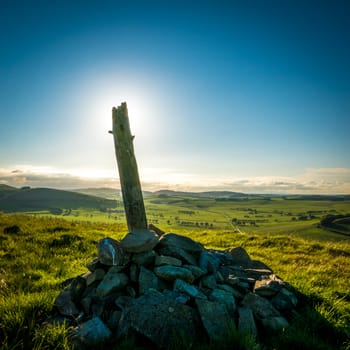 Stones And A Wooden Post At The Summit Of A Hill In Rural Scotland At Sunset