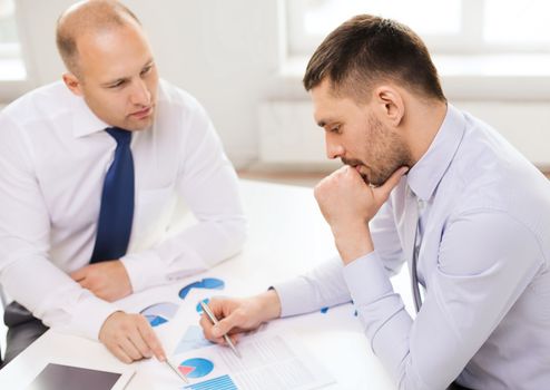 business, technology and office concept - two businessmen with tablet pc computer and papers having discussion in office