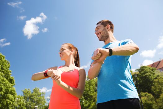 fitness, sport, training, technology and lifestyle concept - two smiling people with heart rate watches outdoors