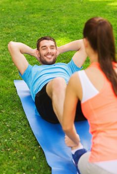 fitness, sport, training, teamwork and lifestyle concept - smiling man with personal trainer doing exercises on mat outdoors