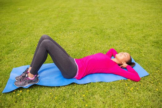 fitness, sport, training, park and lifestyle concept - smiling african american woman doing exercises lying on mat outdoors