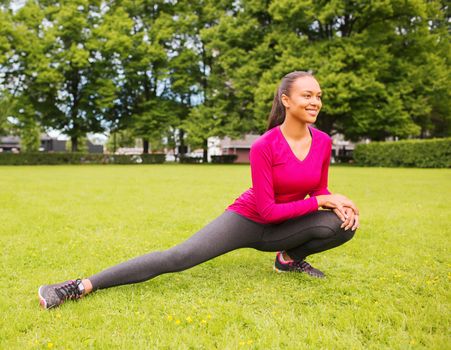 fitness, sport, training, park and lifestyle concept - smiling african american woman stretching leg outdoors