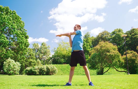 fitness, sport, training and lifestyle concept - smiling man stretching hand outdoors