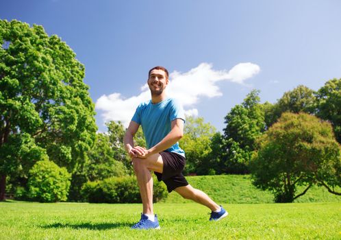 fitness, sport, training and lifestyle concept - smiling man stretching leg outdoors