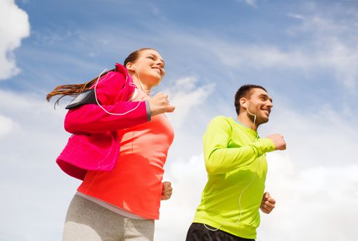 fitness, sport, friendship and lifestyle concept - smiling couple with earphones running outdoors