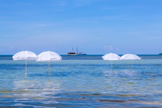 White umbrella on summer tropical beach with sailing boat.