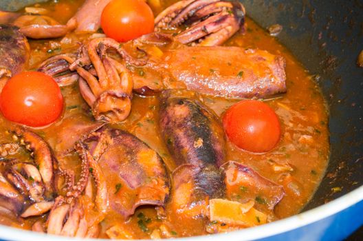 Tasty fish soup with squid, tomato and onion in a large skillet.