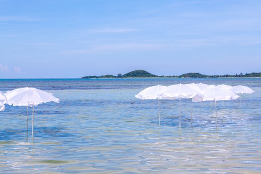 White umbrella on summer tropical beach with sailing boat.