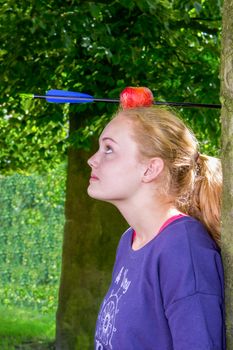 Girl with apple and arrow on her head standing outdoors