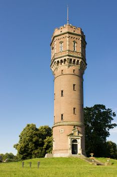 Brick water tower with blue sky and green trees in summer