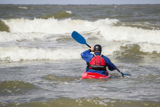 Man paddling in kayak on water of sea with waves