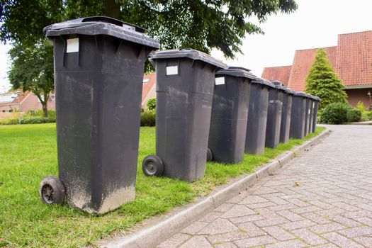 Grey garbage containers in a row standing along street