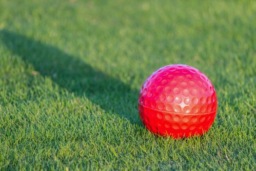 Red golf ball on grass with shadow of evening sun