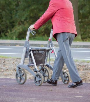 Anonymous elderly person walking with walker along street