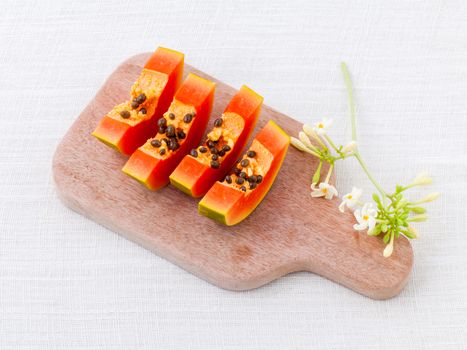 Fresh papaya and papaya slice with papaya leaf on cutting board.