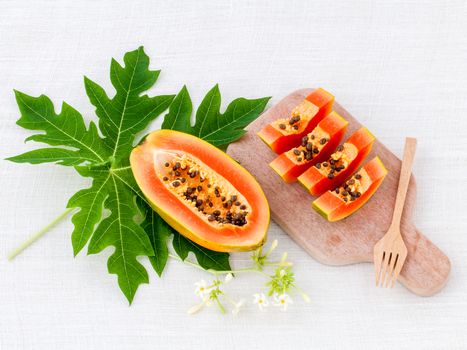 Fresh papaya and papaya slice with papaya leaf on cutting board.