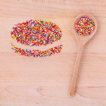 Colourful topping baking in wooden spoon and the shape of macaroons on wooden table.