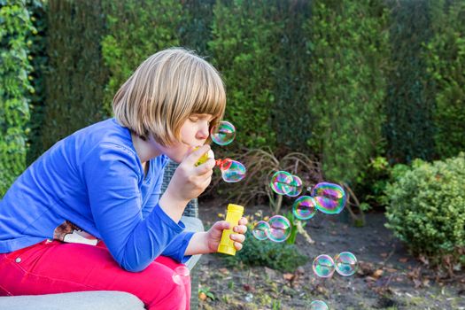 Young dutch girl blowing bubbles from soapy water in garden outdoors