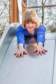 Young caucasian girl lies forward on slide at playground