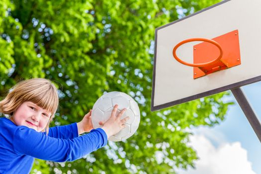 Young caucasian child aiming ball at board with basket at playground of school