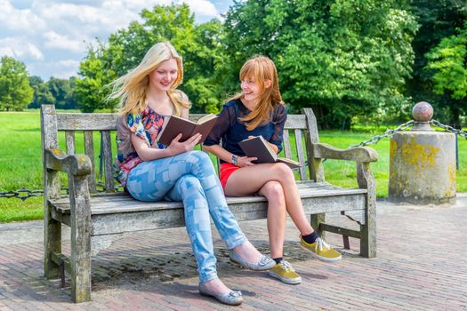 Caucasian teenage girls sitting on wooden bench in green park reading books