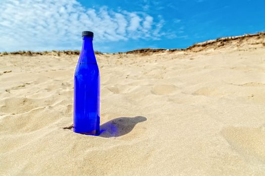 Blue water bottle standing upright in dry yellow sand like desert