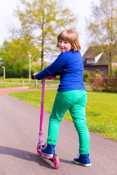 Young caucasian girl with pink scooter on street looking back