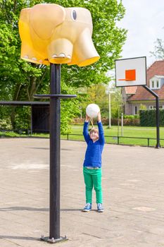 Young european girl aiming ball at basket like elephant on playground of school