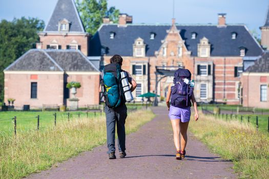 Man and woman with backpacks walking on road to castle in summer vacation