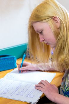 Blonde caucasian schoolgirl making homework at desk