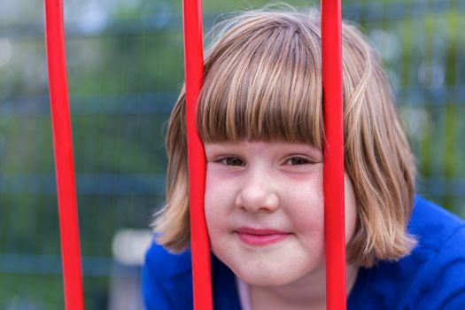 Head of young caucasian girl behind red metal bars