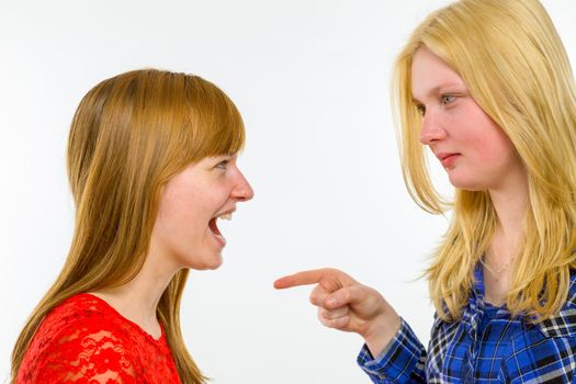 Blonde caucasian girl pointing at red haired girlfriend isolated on white background