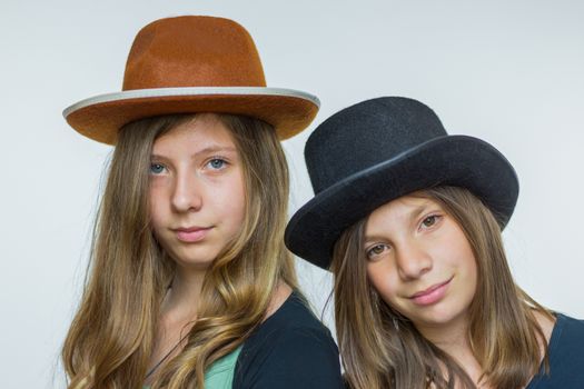 Two european teenage sisters with long hair wearing hats isolated on white background