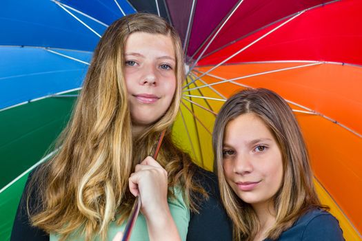 Two caucasian  teenage sisters together under colorful umbrella