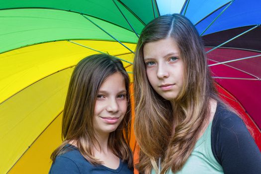Two caucasian teenage sisters under colorful rainbow umbrella with various colors