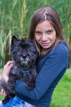 Caucasian teenage girl carrying and hugging black dog on arm in nature