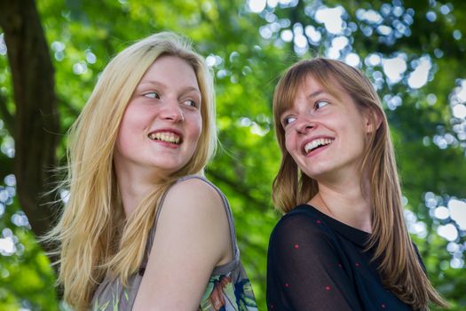 Two long-haired dutch teenage girls laughing to each other with tree background