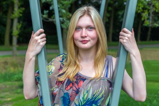 Blonde caucasian teenage girl between green metal tubes in park