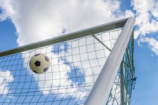 Football shot in corner of goal with blue sky and white clouds